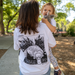 Woman wearing a white t-shirt with a black animal illustration, holding a child in a park.