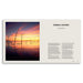 A printed book or magazine spread shown against a white background. The left page features a photograph of a colorful sunset over still water with tree trunks standing in the reflection, and the right page has the title 'FRAMING A CONTINENT' and several text columns on an off-white page.