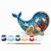 A whale-shaped wooden craft painting kit with an ocean-themed laser-cut design, six small paint pots, and a paintbrush on a white background.