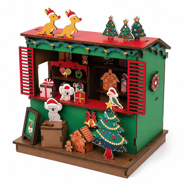 A colorful wooden 3D puzzle building of a Christmas market stall, featuring green walls, a red roof, and various festive decorations including a Christmas tree, gingerbread houses, Santa Koalas, and reindeer on a white background.
