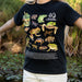 Person wearing a black t-shirt with illustrations of Australian frogs, standing in a natural setting.