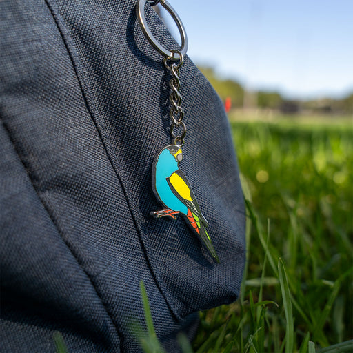 Colorful bird-shaped keychain attached to a dark blue backpack outdoors.