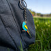 Colorful bird-shaped keychain attached to a dark blue backpack outdoors.