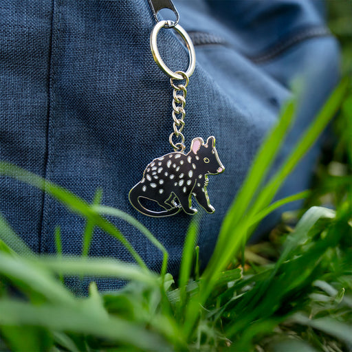 Keychain with a spotted animal design hanging from a blue fabric bag in grass.
