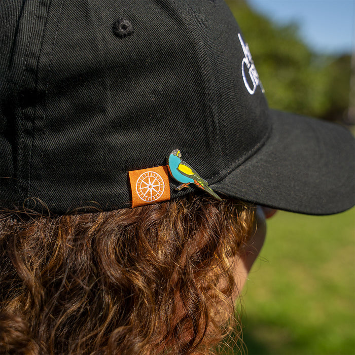 Person wearing a black cap with a bird design and a logo on the brim, outdoors.