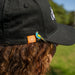 Person wearing a black cap with a bird design and a logo on the brim, outdoors.