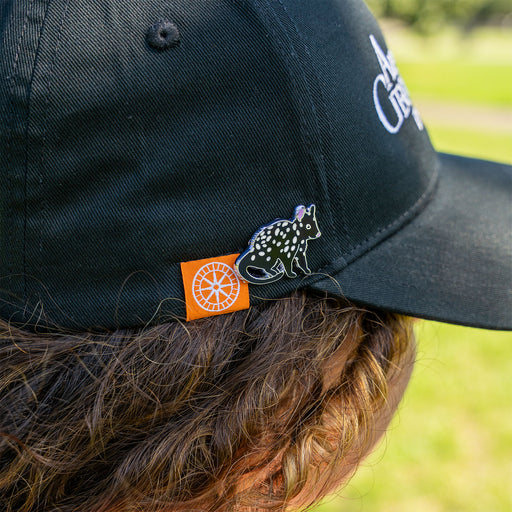 Black cap with a spotted animal design and orange tag worn by a person outdoors.