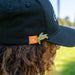 Person wearing a black cap with a turtle logo on a blurred outdoor background