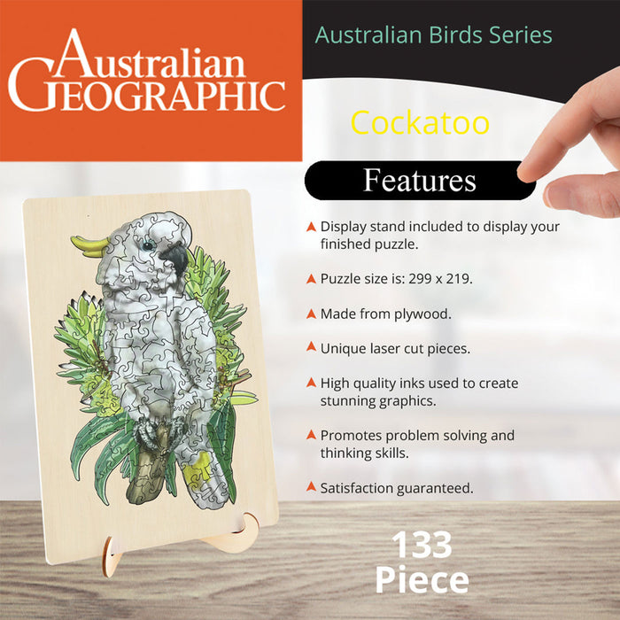Australian Geographic brand Cockatoo puzzle card shown on a small display stand, with a human finger pointing at the right side of the image and feature text beside it. The puzzle artwork shows a cockatoo made of interlocking puzzle pieces over green foliage.
