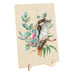 A rectangular wooden plaque or sign on a small wooden display stand, featuring a painted kookaburra perched among green leaves and pink flowers on a light wood background.