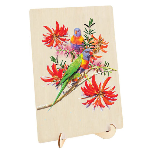 A rectangular wooden plaque or board on a small wooden display stand, featuring a colorful print of two lorikeets among bright red flowers on a light wood background.