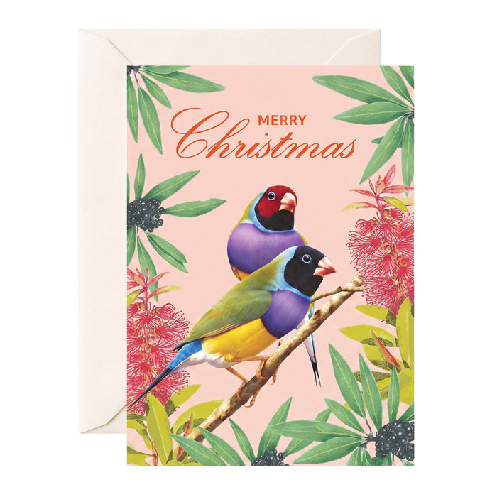 A Christmas greeting card with a light pink background, featuring two colorful Gouldian finches perched among green leaves and pink flowers. The words 'Merry Christmas' are written in orange script at the top.