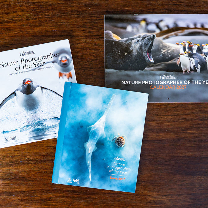 Three Australian Geographic Nature Photographer of the Year products displayed on a dark wooden tabletop, with one open to show the cover and one closed showing the front cover.