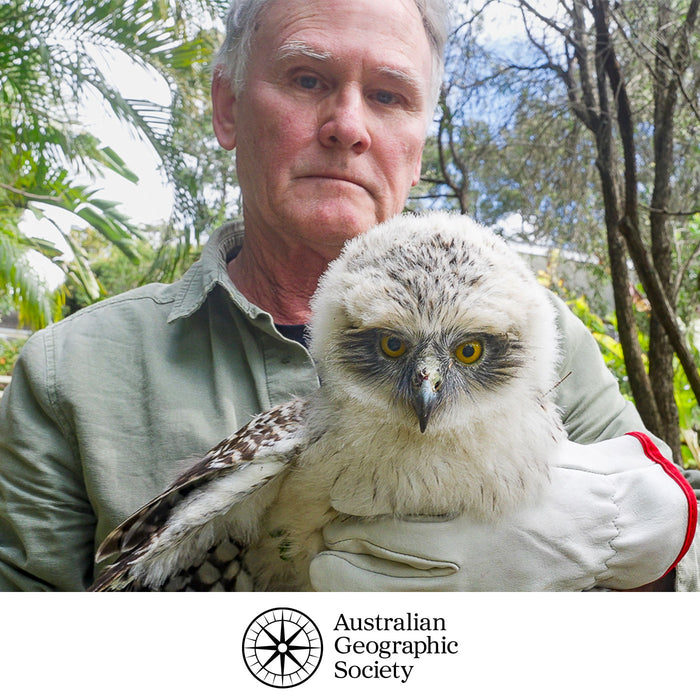 Man holding a large owl with a natural background, featuring the Australian Geographic Society logo.