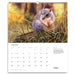 A spiral-bound wall calendar page showing a photographic wildlife scene of a gray and orange rodent in tall grass, with a July 2027 calendar grid and text on the lower white section.