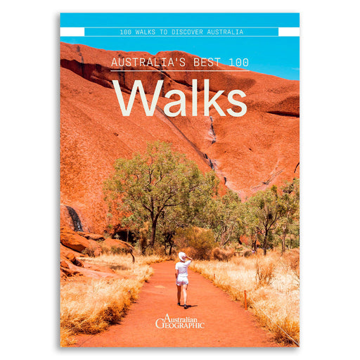 Front cover of the Australian Geographic book '100 Walks to Discover Australia' featuring a scenic photograph of a hiker on a red dirt path with red rock cliffs and trees under a bright blue sky.