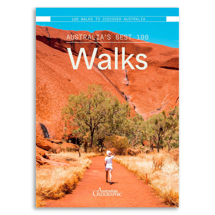 Front cover of the Australian Geographic book '100 Walks to Discover Australia' featuring a scenic photograph of a hiker on a red dirt path with red rock cliffs and trees under a bright blue sky.