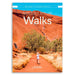 Front cover of the Australian Geographic book '100 Walks to Discover Australia' featuring a scenic photograph of a hiker on a red dirt path with red rock cliffs and trees under a bright blue sky.
