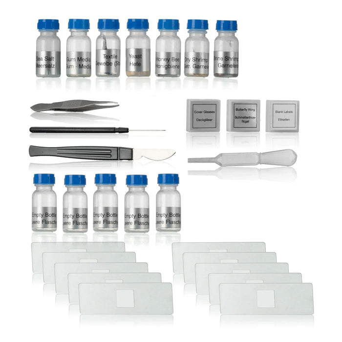 A microscope specimen preparation kit arranged on a white reflective background, including multiple small vials with blue caps, glass slides, forceps, a needle, a spatula, and labeled glass covers.