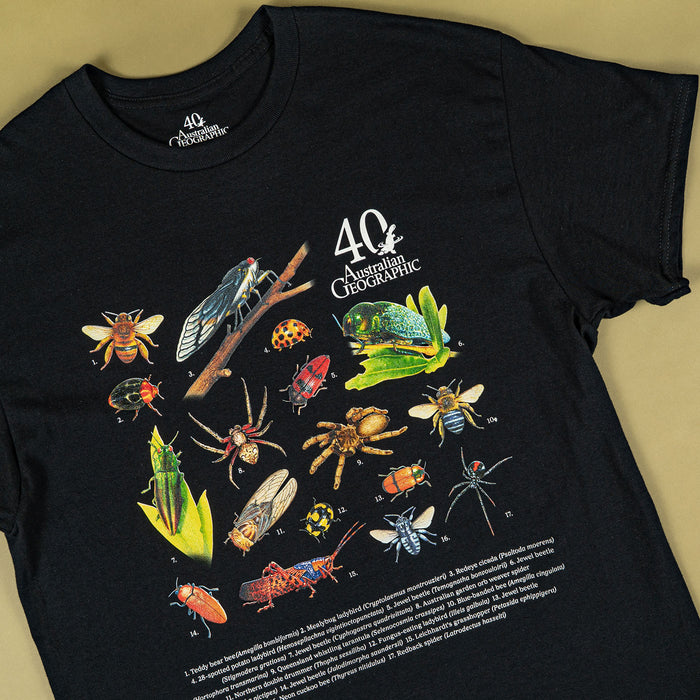 A black short-sleeve graphic T-shirt laid flat on a warm beige background. The shirt features a large colorful print of various insects and spiders, with the text '40th Anniversary' and 'Australian Geographic' on the chest.