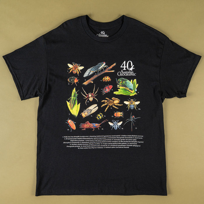 A black short-sleeve graphic t-shirt laid flat on a solid tan background. The front of the shirt features a colorful scientific-style illustration of various insects, spiders, and other bugs, alongside the text '40 Australian Geographic' and a block of smaller descriptive text at the bottom.