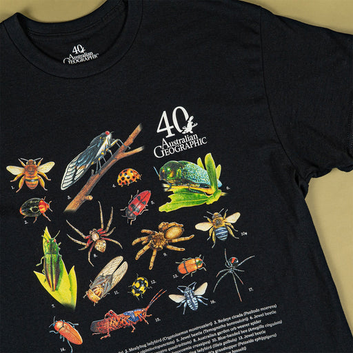 A black short-sleeve graphic T-shirt laid flat on a beige background, featuring a large illustrated collection of insects and the text '40 Australia Geographic' on the chest.