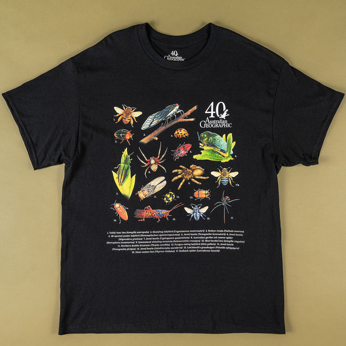 A black short-sleeve graphic t-shirt laid flat on a solid tan background. The front of the shirt features a colorful scientific-style illustration of various insects, spiders, and other bugs, alongside the text '40 Australian Geographic' and a block of smaller descriptive text at the bottom.