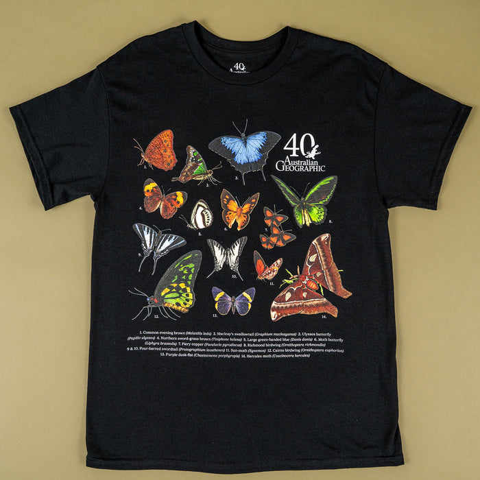 A black short-sleeve graphic T-shirt laid flat on a beige background, featuring a large printed collage of colorful butterflies and moths with the text '40 Years of Australian Geographic' and smaller descriptive text below.