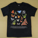 A black short-sleeve graphic T-shirt laid flat on a beige background, featuring a large printed collage of colorful butterflies and moths with the text '40 Years of Australian Geographic' and smaller descriptive text below.
