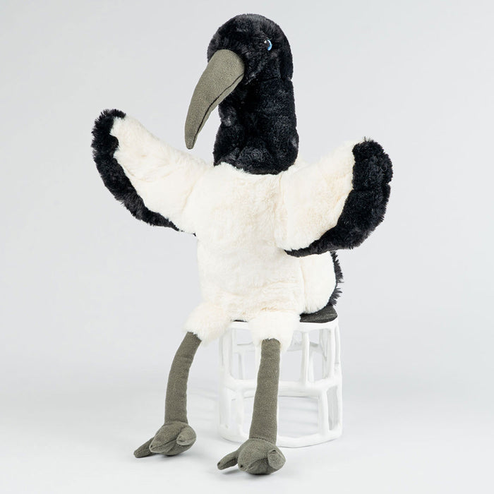 Plush toy ibis on a clear glass stand against a white background