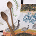 Wooden spoons on a marble surface with a decorative towel featuring emus in the background.