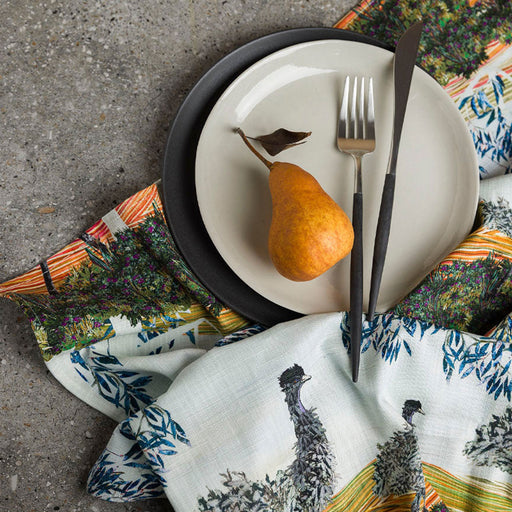 Dinner setting with a pear on a plate, cutlery, and patterned napkins.
