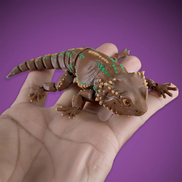 Toy bearded dragon held in a hand against a purple background