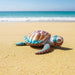 Toy turtle on a sandy beach with ocean in the background