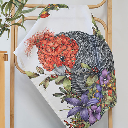 Decorative pillow with a gang gang and floral design on a wooden rack.