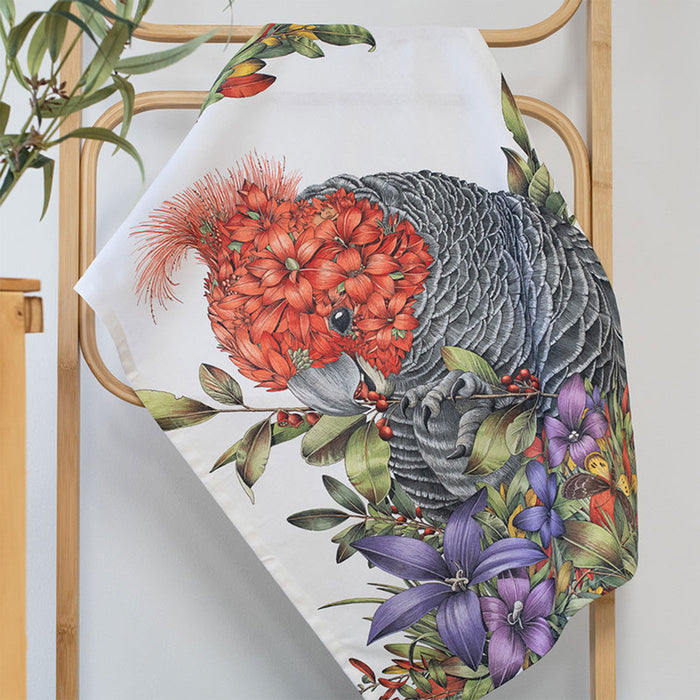 Decorative pillow with a gang gang and floral design on a wooden rack.