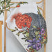Decorative pillow with a gang gang and floral design on a wooden rack.