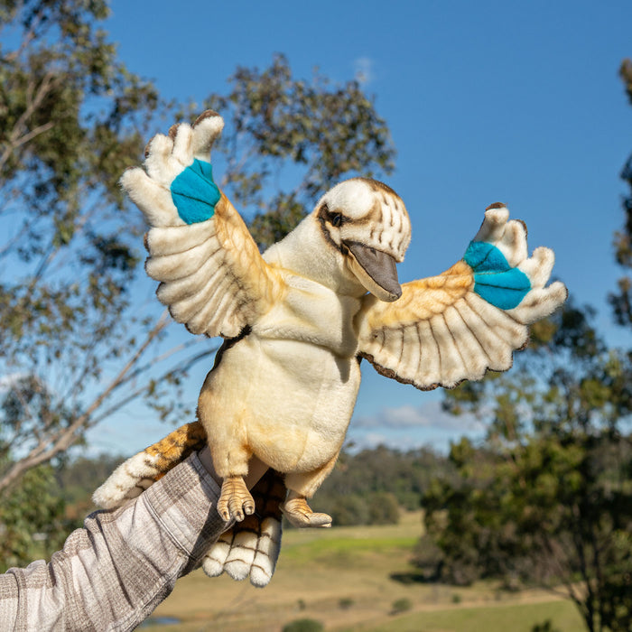 Plush toy penguin with outstretched wings held by a person against a natural background