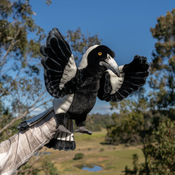 Black and white bird puppet on a person's hand with a natural landscape background