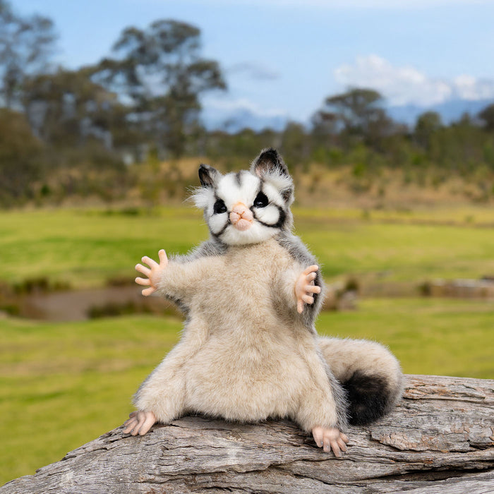 Stuffed animal sugar glider on a log with a natural landscape background