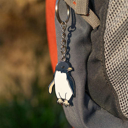 Penguin keychain attached to a gray bag with a blurred natural background