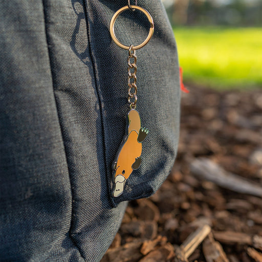 Keychain with a platypus design attached to a gray bag outdoors.