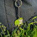 Green frog keychain on a gray fabric background with grass in the foreground