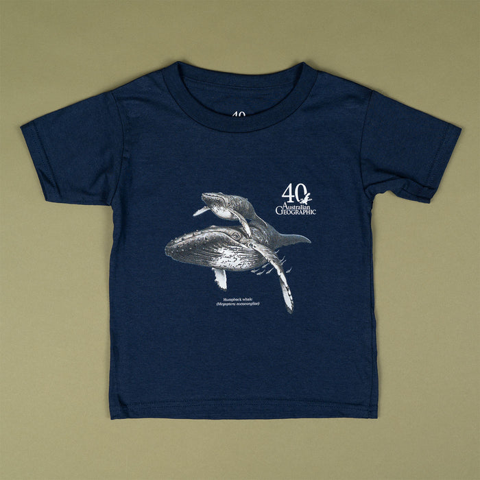 A navy blue short-sleeve t-shirt with a graphic print of a humpback whale and the text '40 Years Australian Geographic' on the front, laid flat on a solid olive-beige background.