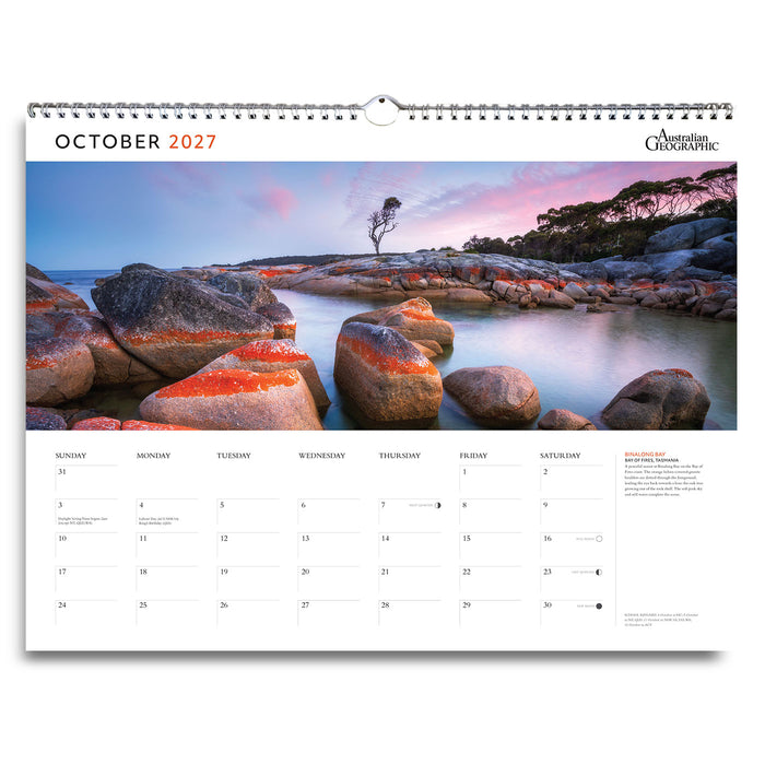 A single-page October 2027 wall calendar spread from Australian Outback, featuring a scenic coastal landscape print with large rocks, calm water, and a pink-and-blue sunset sky. The calendar includes a spiral binding at the top and a monthly calendar grid with weekday columns and a small text sidebar on the right.
