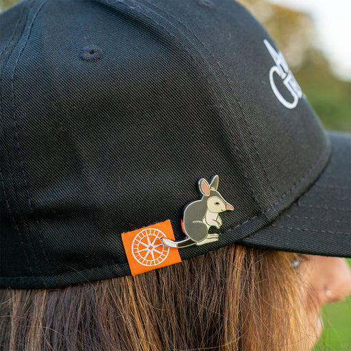 Black cap with a bilby pin and orange label worn by a person outdoors