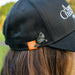 Black cap with orange logo and black cockatoo pin worn by a person outdoors