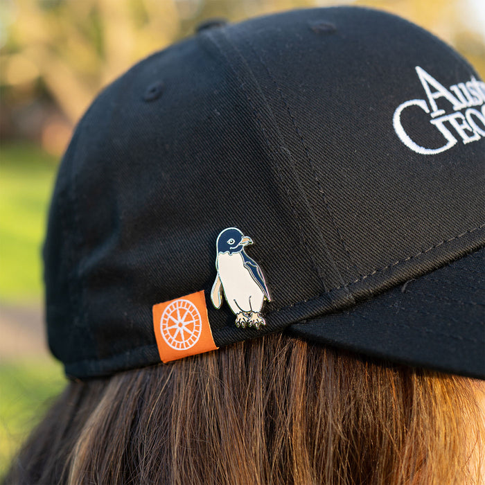 Black cap with a penguin pin and logo on a blurred natural background