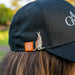 Person wearing a black cap with a kangaroo pin and logo on the back, outdoors.