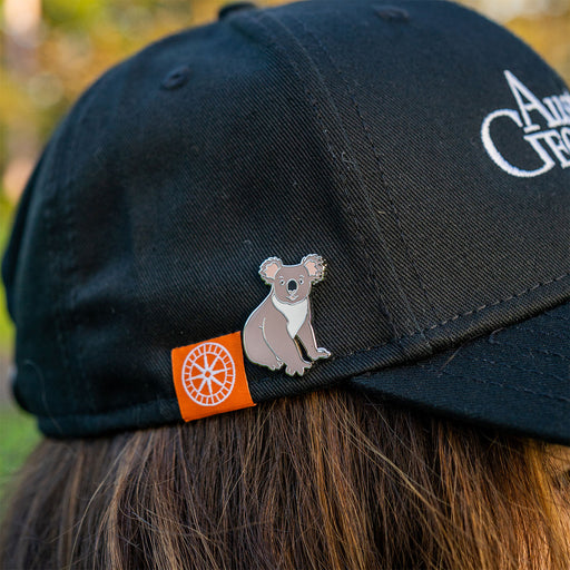 Black cap with a koala pin and logo on a blurred natural background